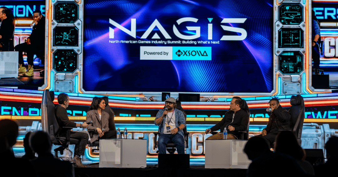 A panel discussion on stage at NAGIS (North American Games Industry Summit), sponsored by Xsolla. Five panelists sit in chairs facing each other on stage, with one speaking into a microphone, in front of a large screen displaying the NAGIS logo and event branding.