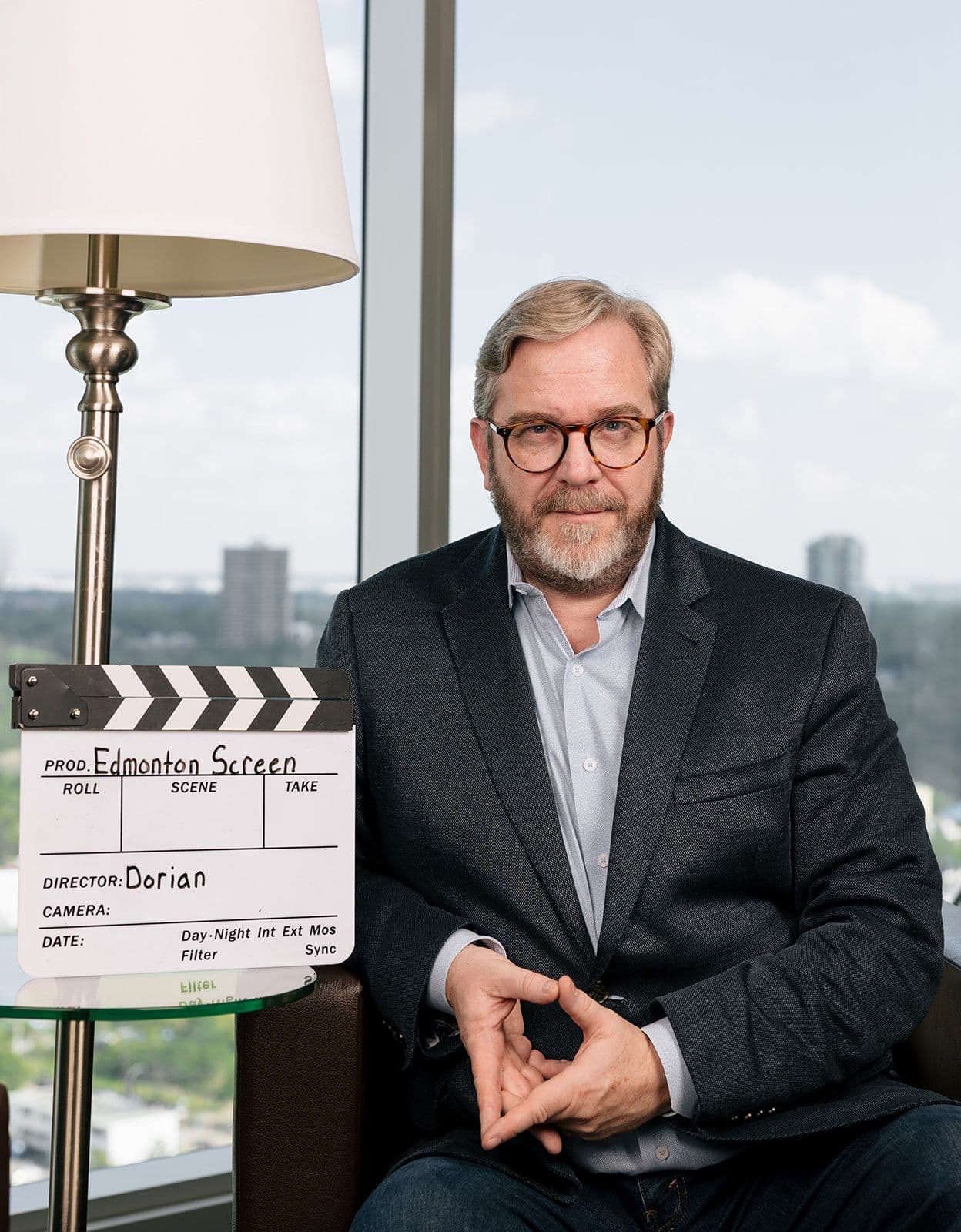 Edmonton Screen Film Commissioner, Dorian Rowe, seated with an Edmonton Screen clapperboard labeled beside him.