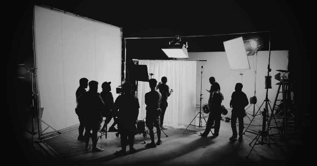 Crew members on a film set, gathered around lighting and camera equipment.