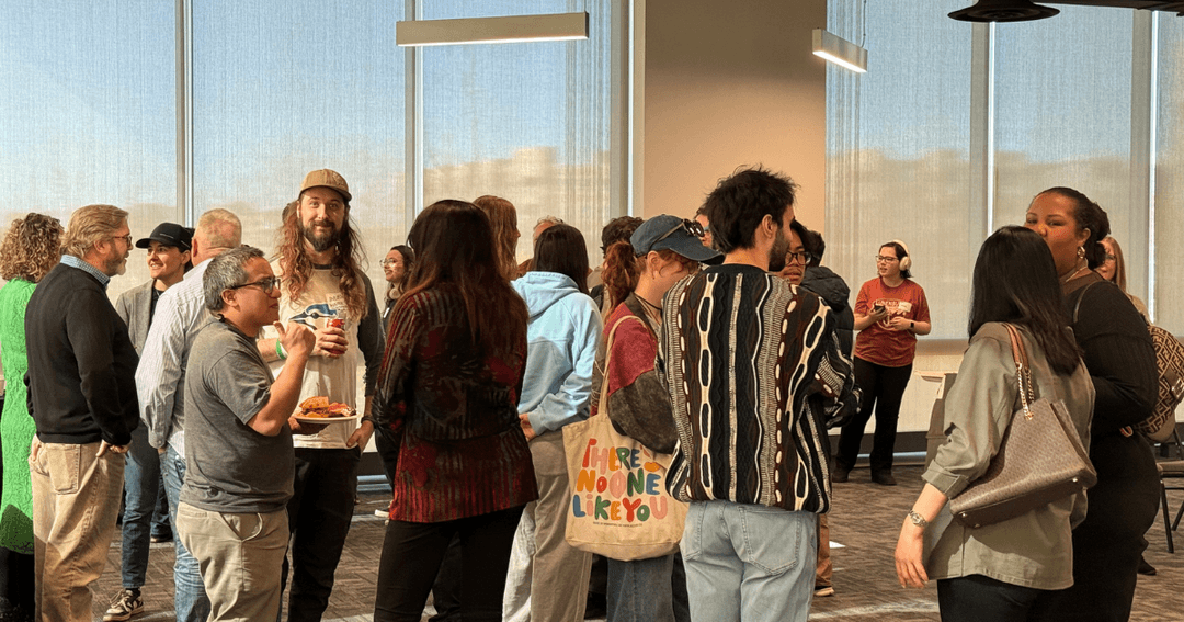 A diverse group of film and media industry professionals networking at an indoor Edmonton Screen community event, with large windows in the background.