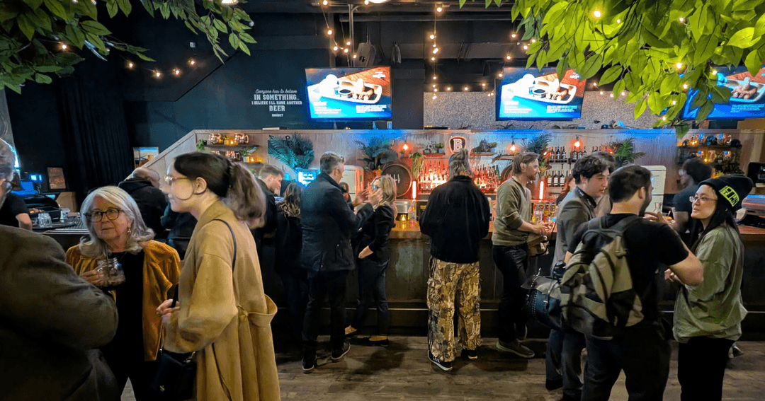 Guests mingle along a long wooden bar under string lights and leafy branches at The Banquet Bar in Edmonton.