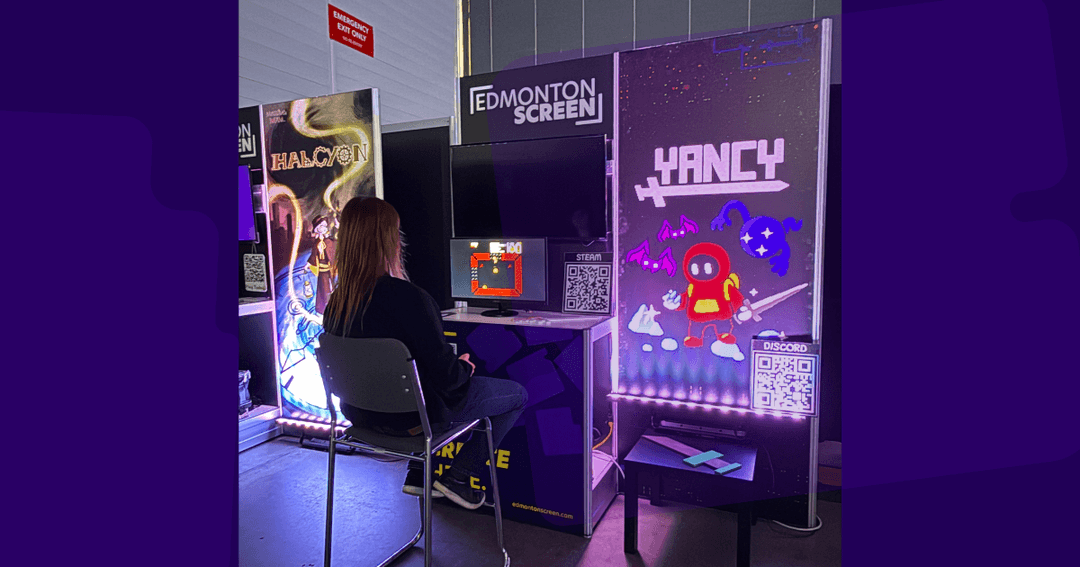 A person attending NAGIS 2026 plays YANCY at Edmonton Screen's booth, with the game's title art and a Steam QR code displayed on the wall beside her.