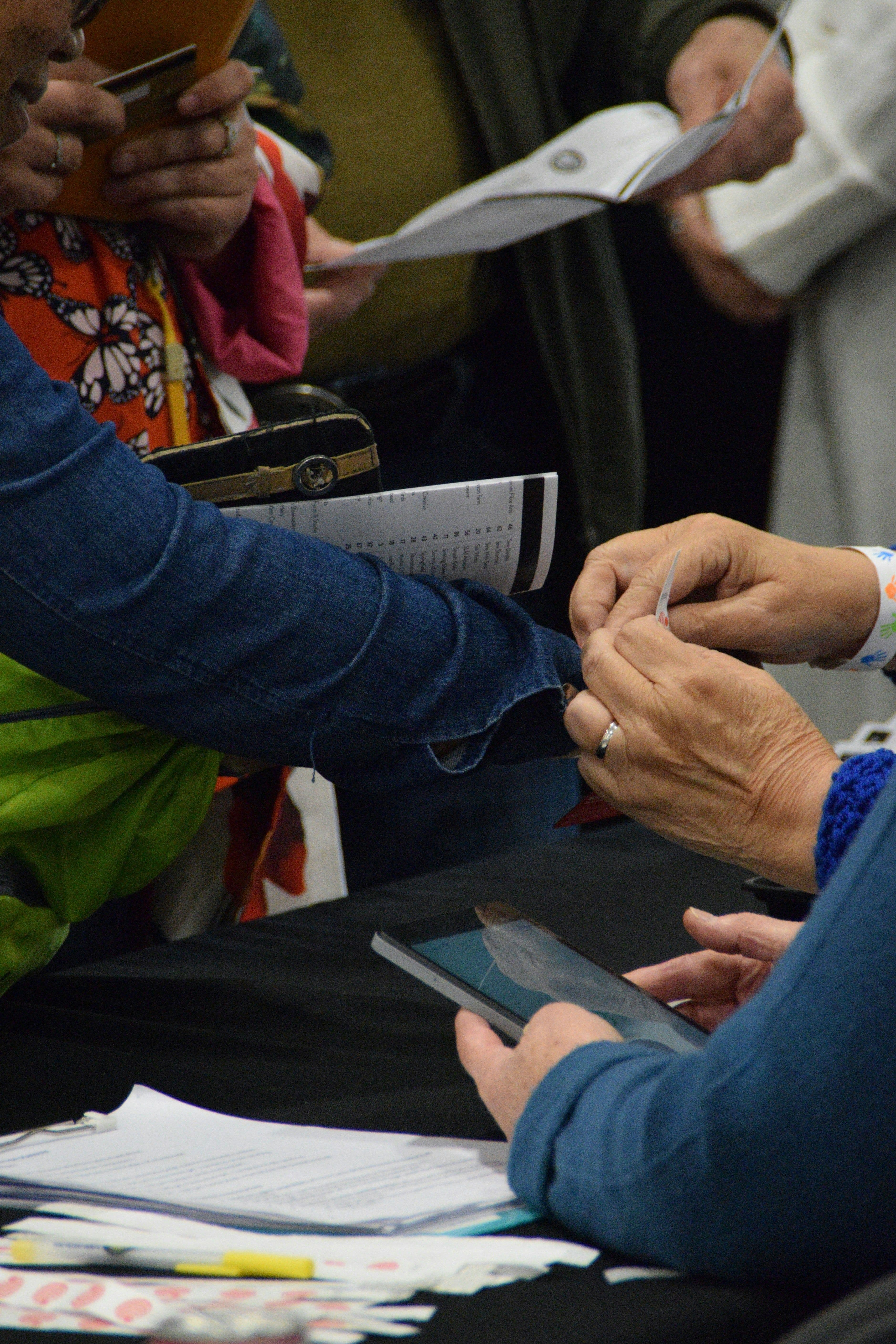 A pair of hands putting on a wristband on a person attending an event.